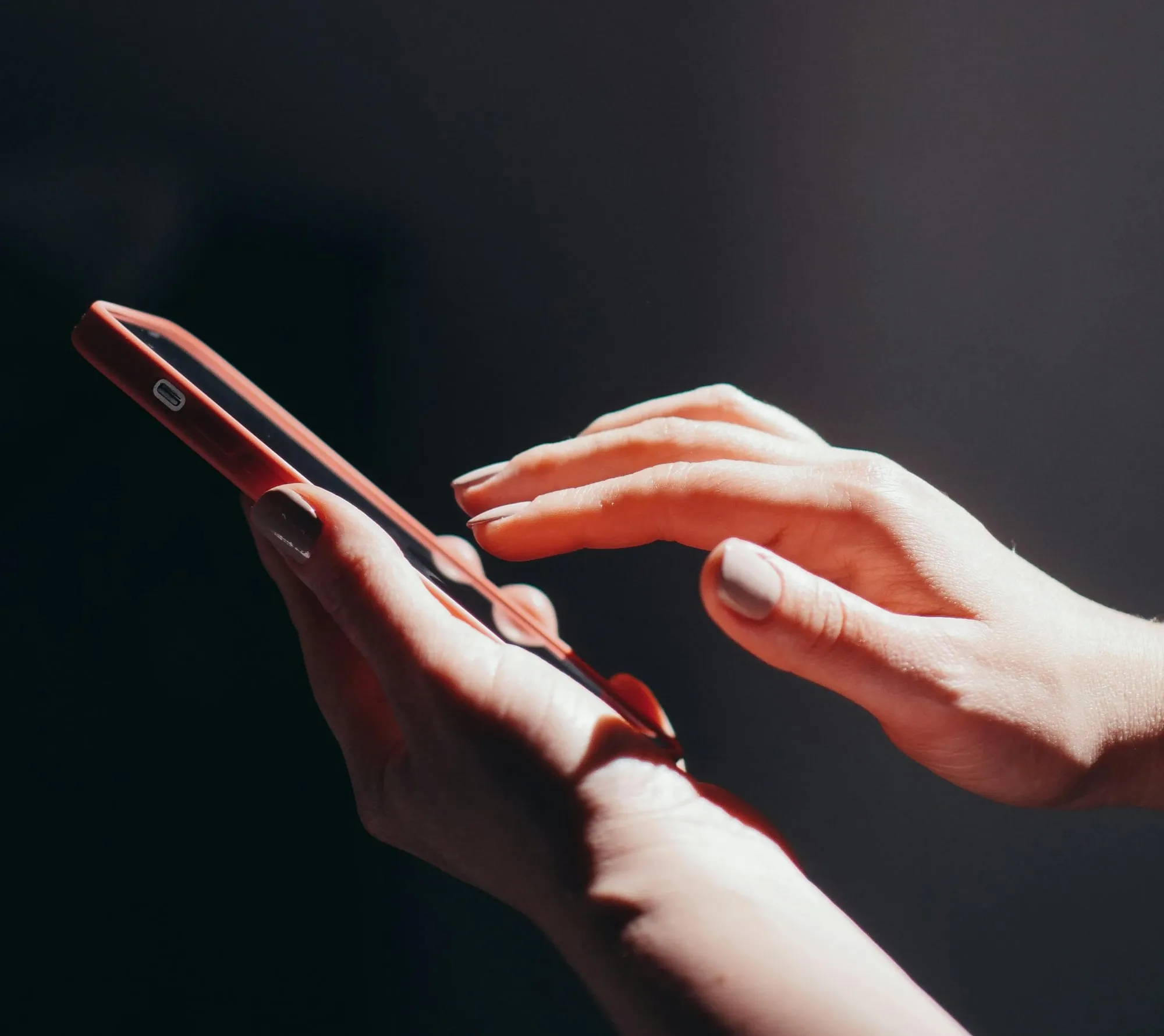 A hand reaching to tap a smartphone held in warm light against a dark background