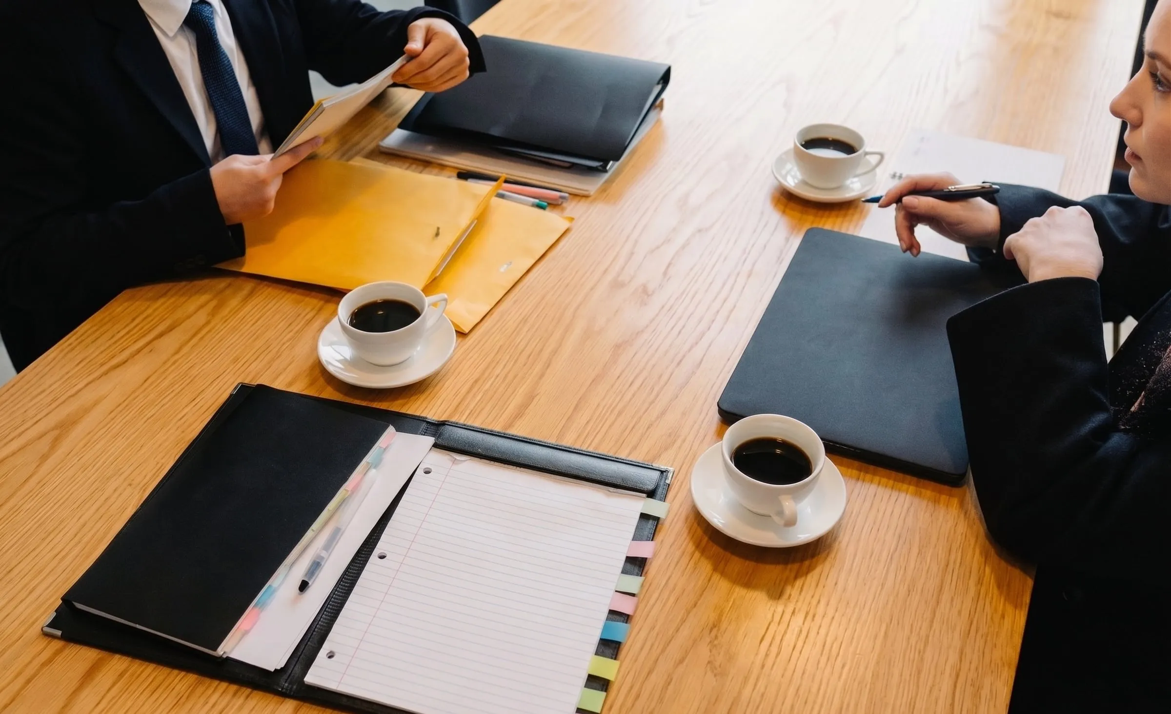 Two professionals reviewing documents across a boardroom table over coffee